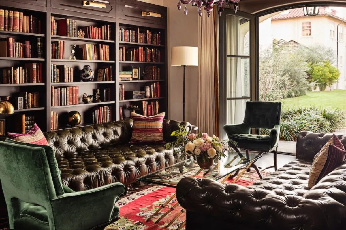 Cozy library lounge with leather chesterfield sofas, bookshelves and garden view through arched doors