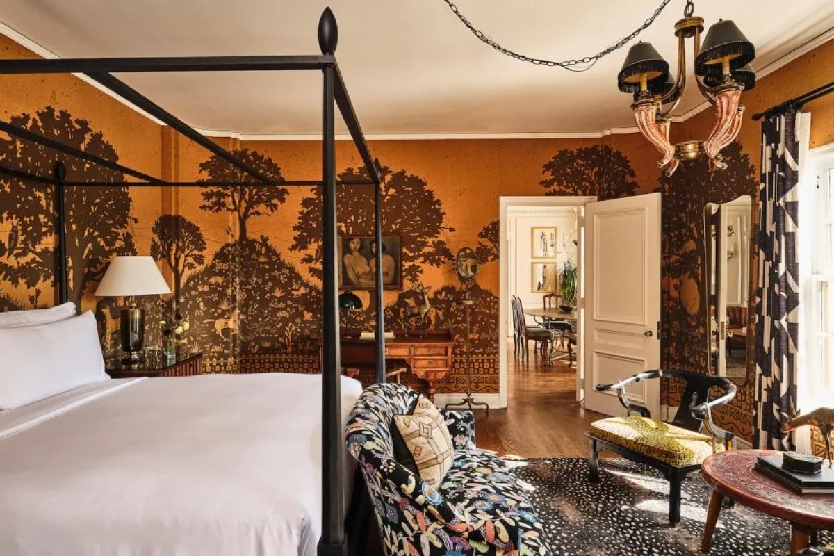 Guest bedroom with four-poster black bed, bold tree-patterned wallpaper and eclectic furnishings