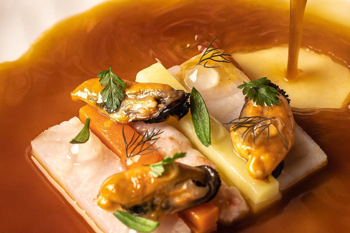 Plated seafood dish with mussels, shrimp, and vegetables drizzled with a glossy sauce.