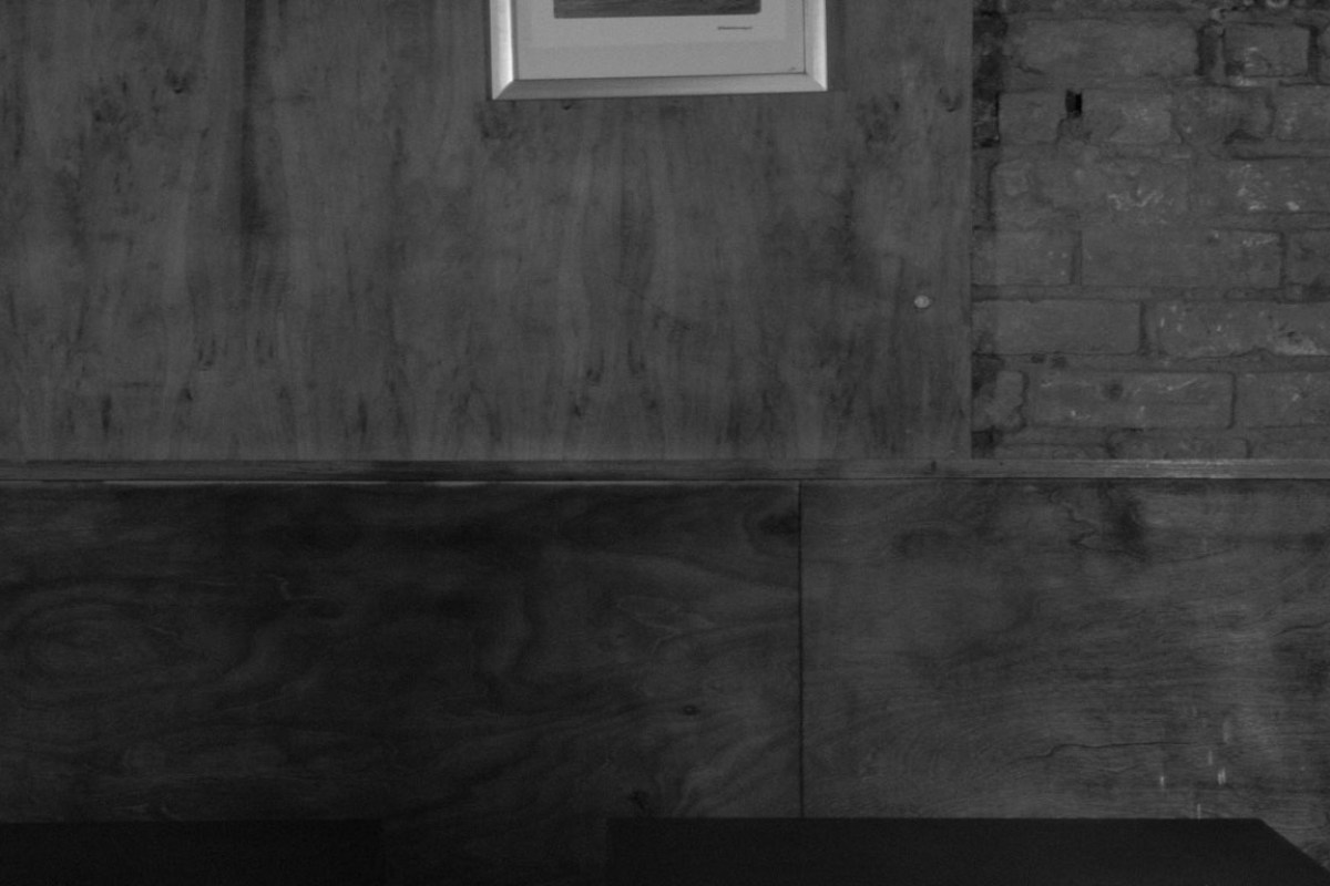 Black and white detail of a plywood-paneled wall with a small framed picture and exposed brick