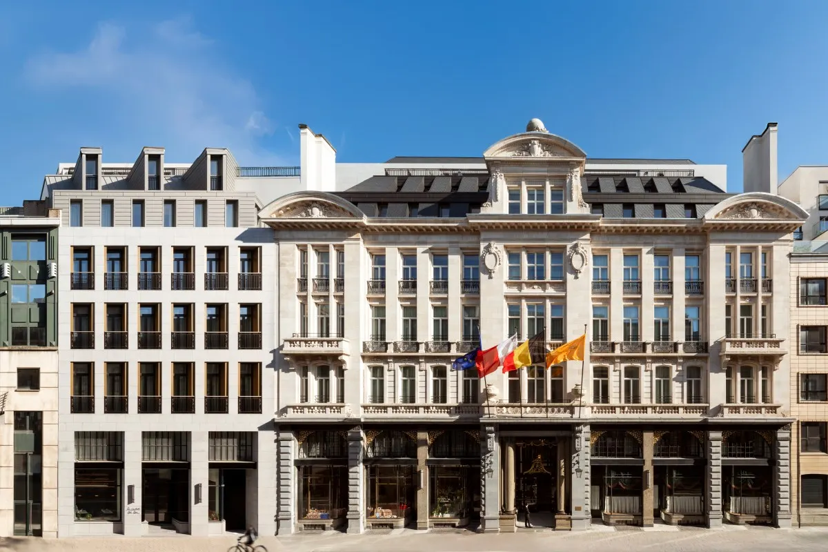 Full façade of the Corinthia Grand Hotel Astoria Brussels, ornate stone building with flags under a blue sky