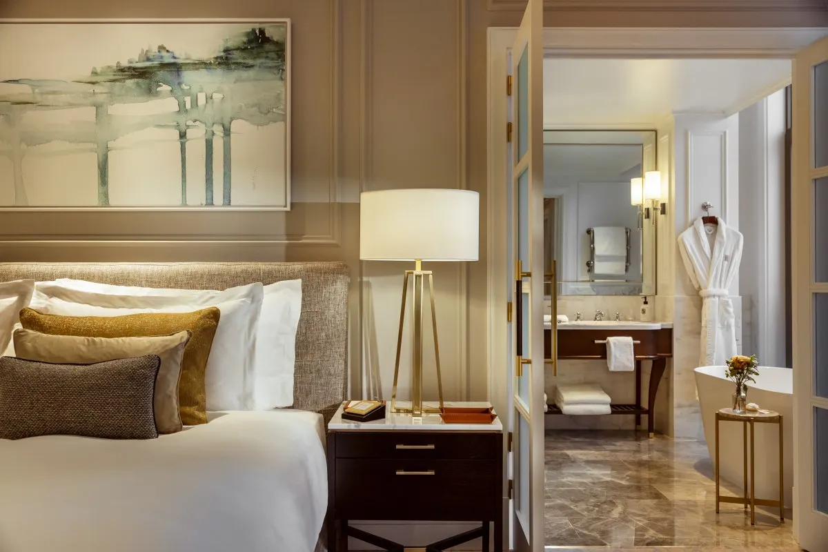 Hotel guest room bed with elegant decor and view into marble bathroom with bathtub