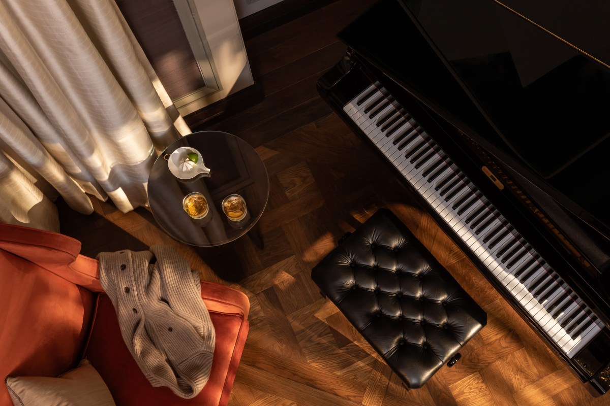 Overhead view of a suite's sitting area with a grand piano, leather bench, armchair and drink table