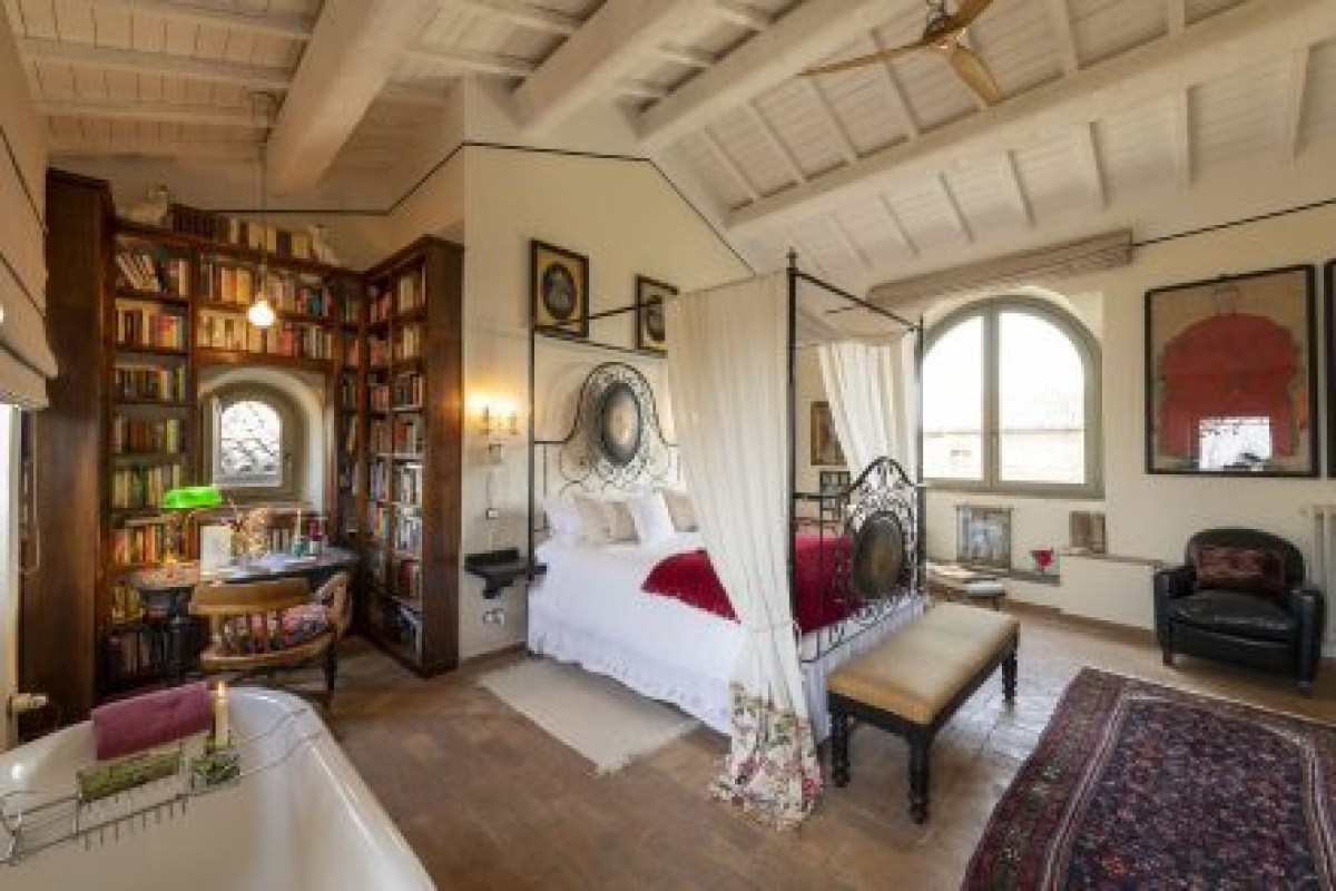 Elegant guest suite with four-poster iron bed, library shelves, arched window, and clawfoot bathtub