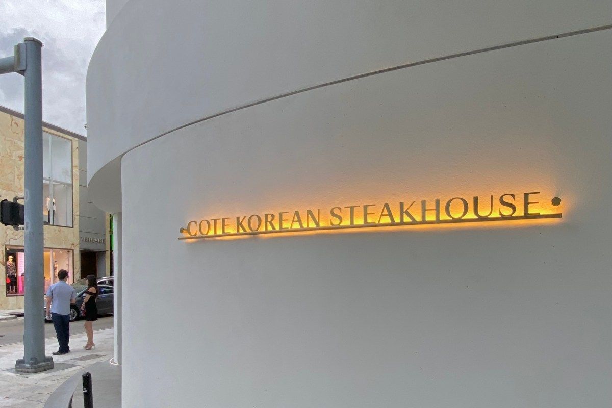 Exterior of Cote Korean Steakhouse in Miami Design District, curved white facade with backlit sign.