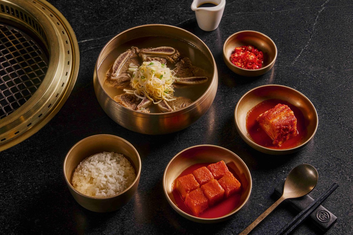 Overhead shot of Korean dishes in brass bowls including soup, rice, kimchi and radish on a dark table