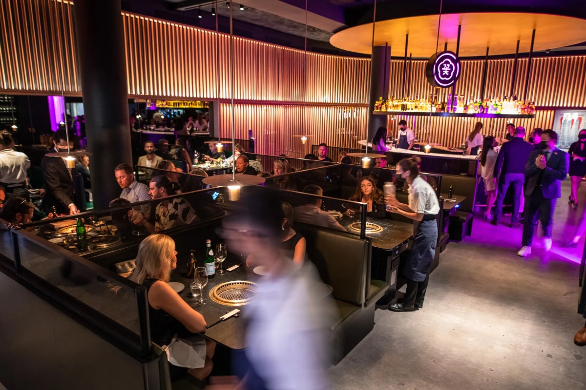 Interior dining room of Cote with booth seating, grill tables, bar and neon sign in background