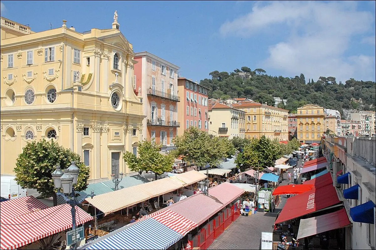 Striped awnings over the market on Cours Saleya in Nice with the yellow Chapelle de la Miséricorde and the hill behind