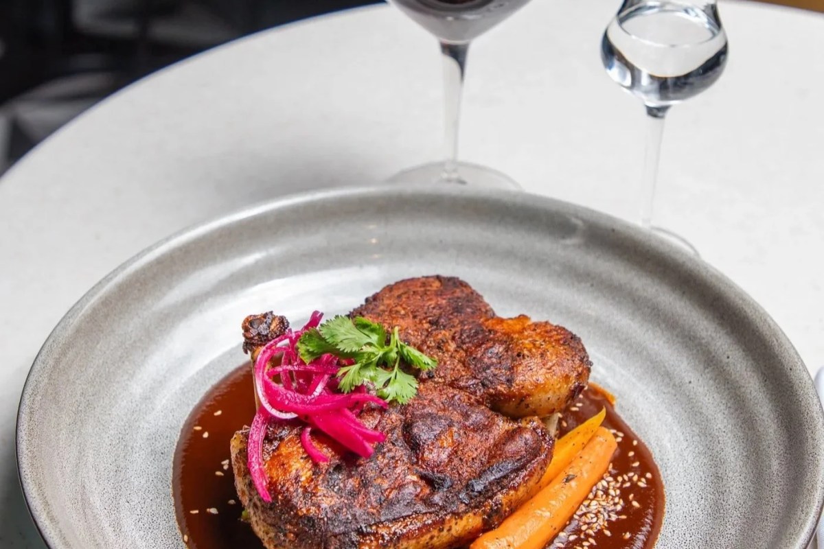 Plated roasted chicken dish with pickled onions, carrots, and wine glasses