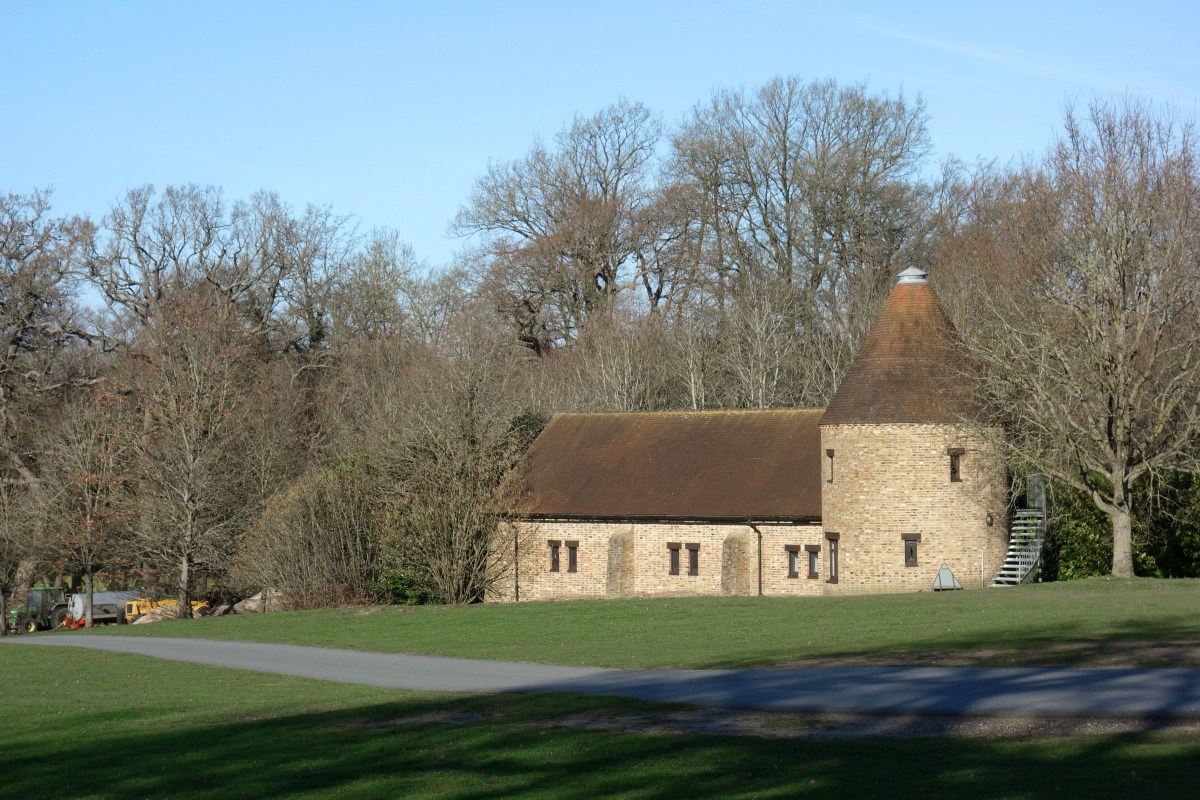 Brick estate building with round turret roof amid trees within Coworth Park grounds, possibly a converted barn or outbuilding used by the hotel.