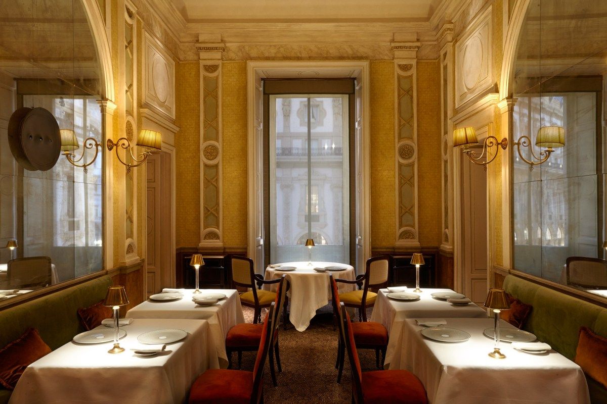 Elegant dining room with white-clothed tables, gilded sconces, and a tall window overlooking the Galleria's arcade.
