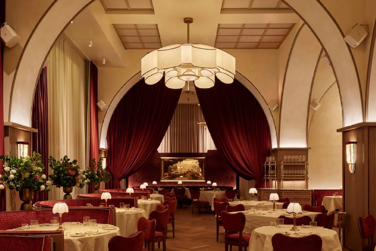 Arched dining room with red velvet curtains, booths, and gold artwork at Crane Club