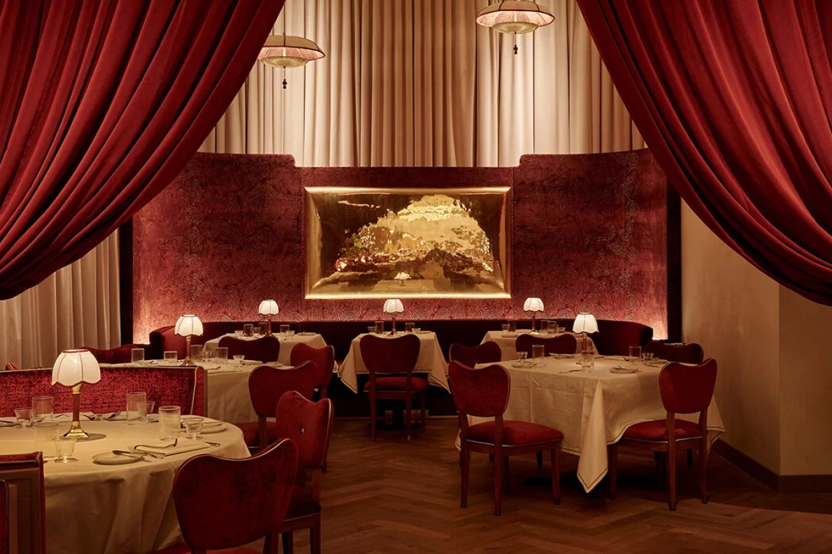 Dining room view with red curtains, booths, and gold artwork panel at Crane Club