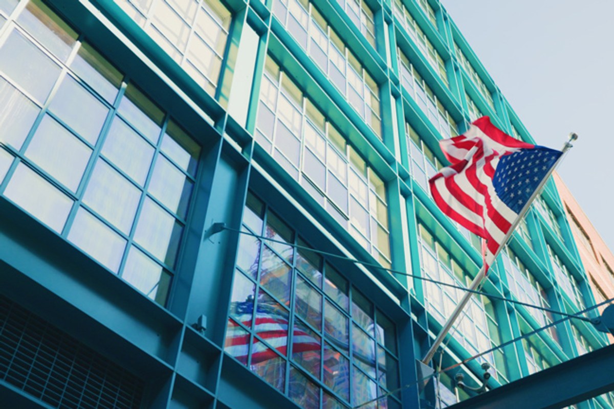 Low-angle view of the Crosby Street Hotel's teal-framed glass façade with an American flag waving in front