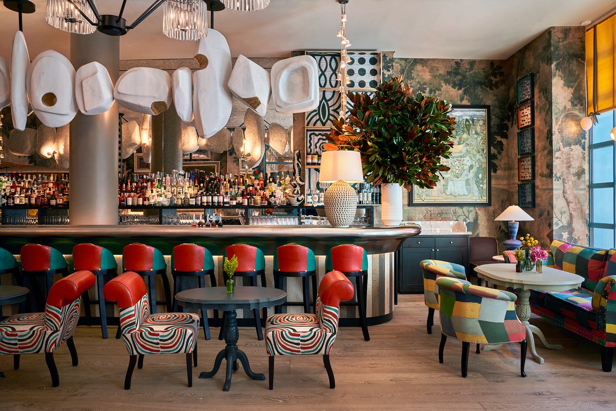 Colorful hotel bar lounge with curved bar, red leather stools, patterned armchairs and sculptural lighting