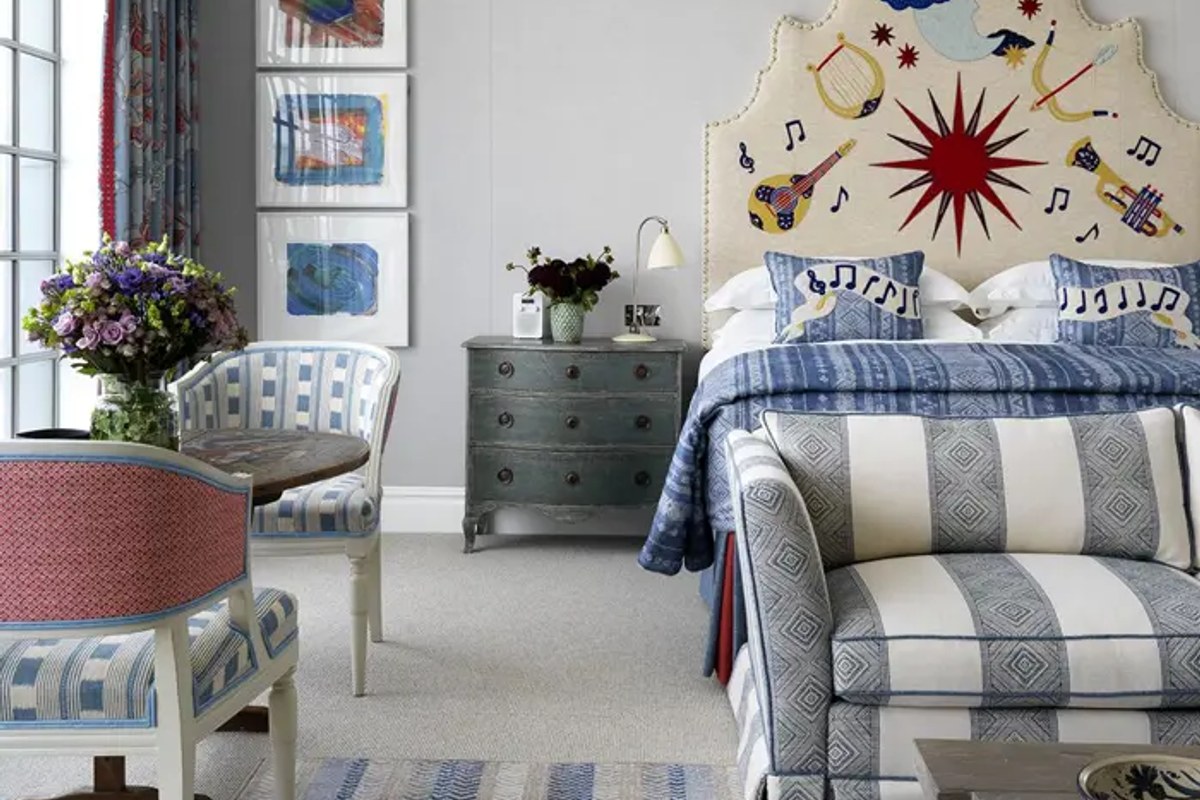 Guest room with striped sofa, patterned headboard with musical motif, antique chest and floral bouquet