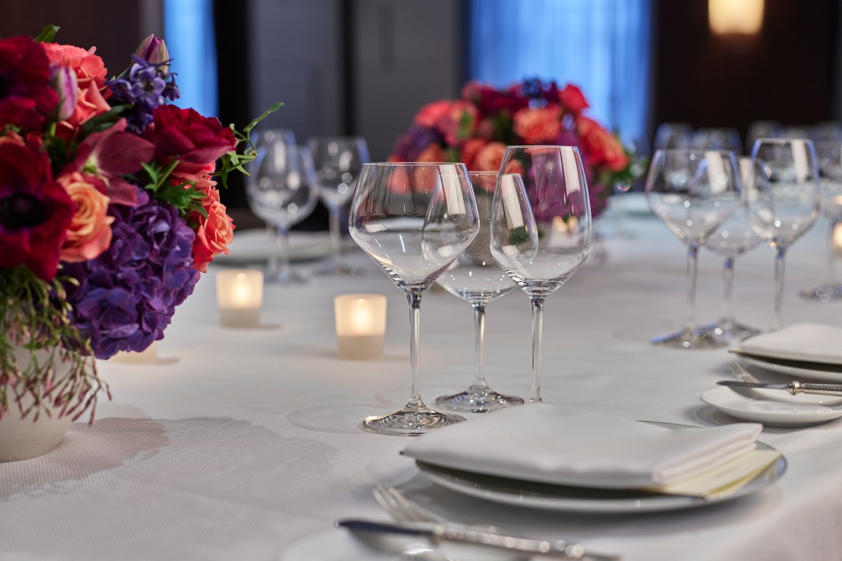 Elegant laid table with wine glasses, candles, and colorful floral centerpieces at a fine dining restaurant.