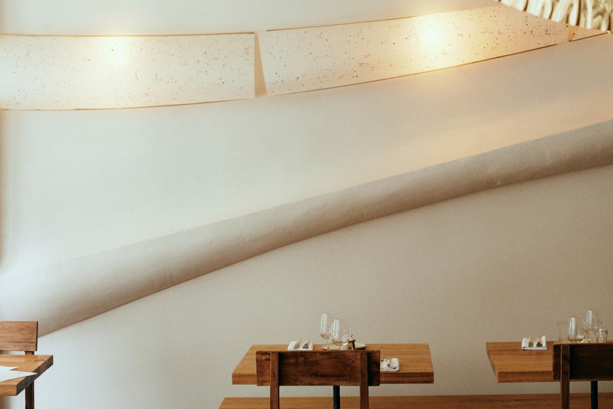 Restaurant dining room with wooden tables, place settings, curved plaster wall and hanging paper light fixtures
