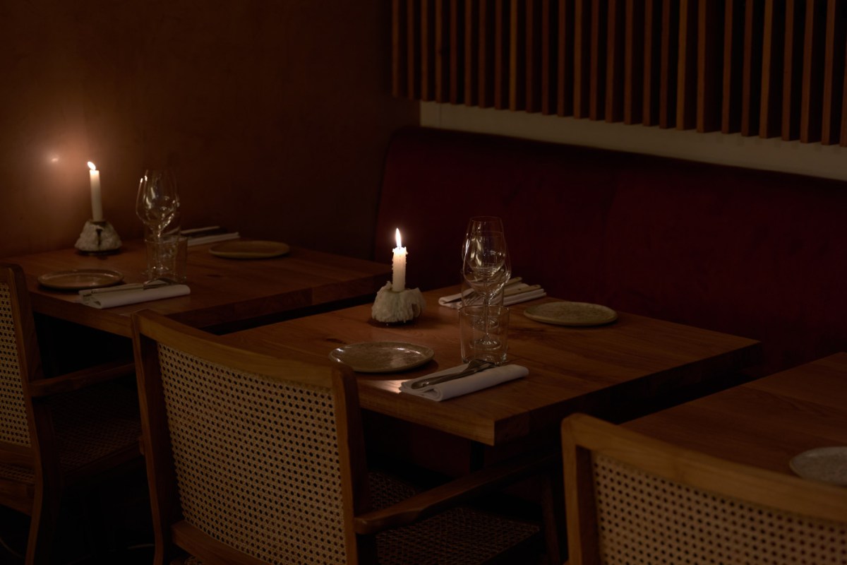 Dim, candlelit dining room with wood tables, cane-back chairs, red banquette seating and laid place settings
