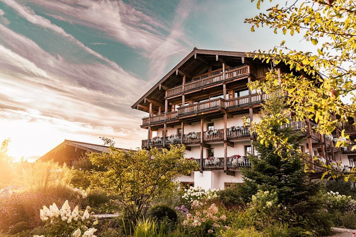 Traditional Bavarian chalet-style hotel building with wooden balconies and flowers, surrounded by lush garden at sunset