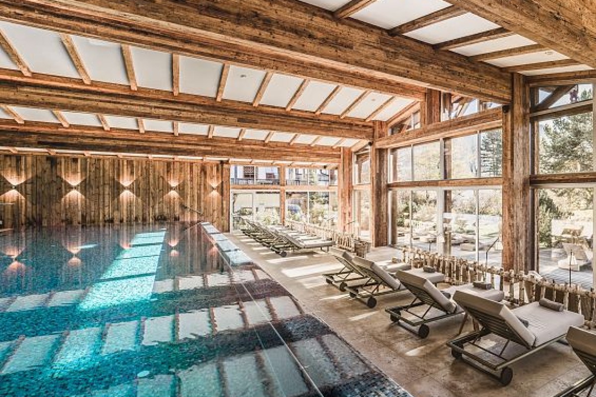 Indoor hotel swimming pool with wooden beam ceiling and loungers beside large windows