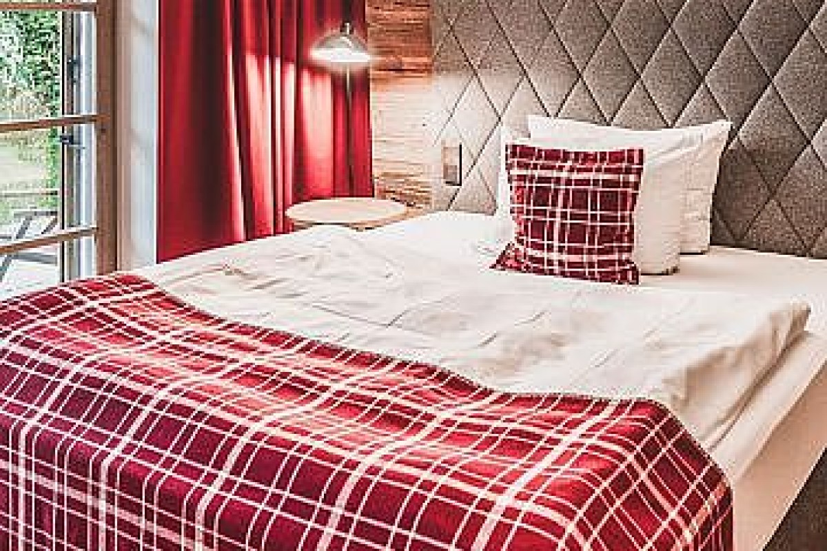 Hotel guest room bed with red plaid blanket and pillows near a window