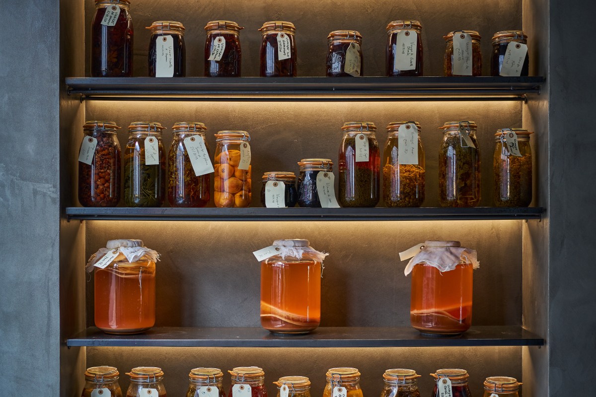 Shelves of jarred preserves and ferments lit against a dark wall inside the restaurant