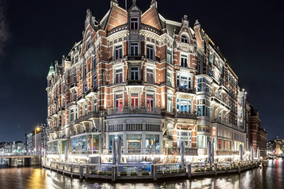Night view of De L'Europe Amsterdam hotel facade lit up, with canal and terrace in foreground
