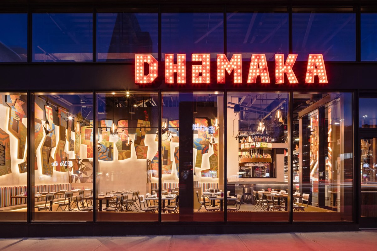 Dhamaka restaurant exterior at dusk with illuminated red marquee sign and view into dining room