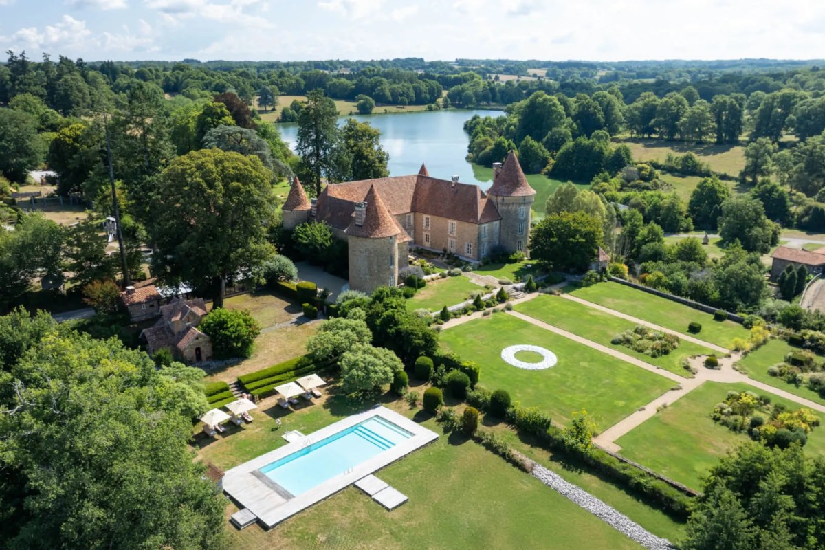 Aerial view of the château with turrets, swimming pool, manicured lawns and lake in the background