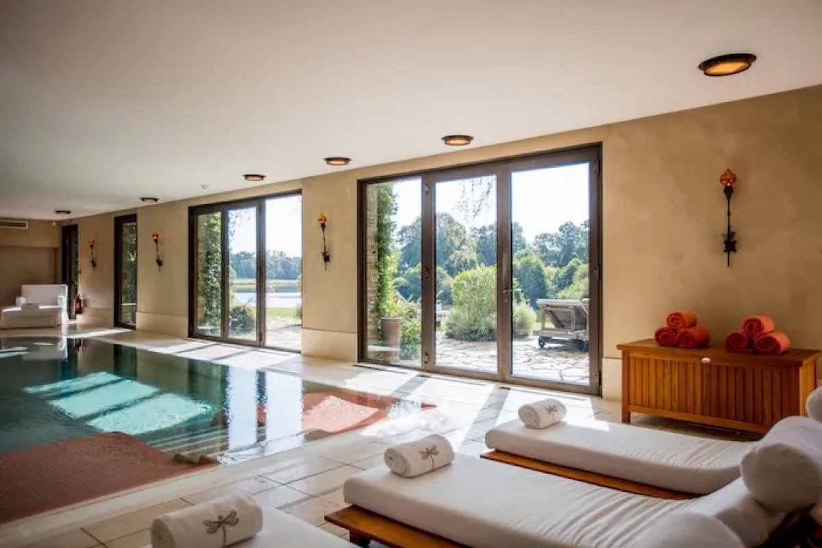 Indoor spa pool with glass doors opening to lake view, lounge chairs with rolled towels