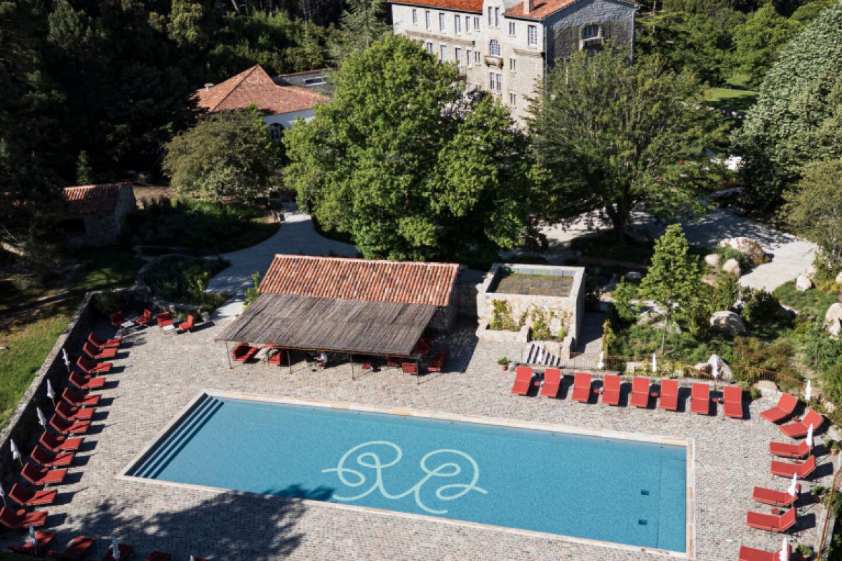 Aerial view of stone hotel building with pool, red lounge chairs, and surrounding greenery