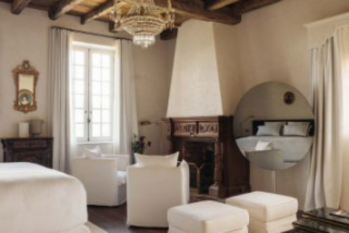 Suite with fireplace, round mirror behind bed, exposed wood beam ceiling and chandelier