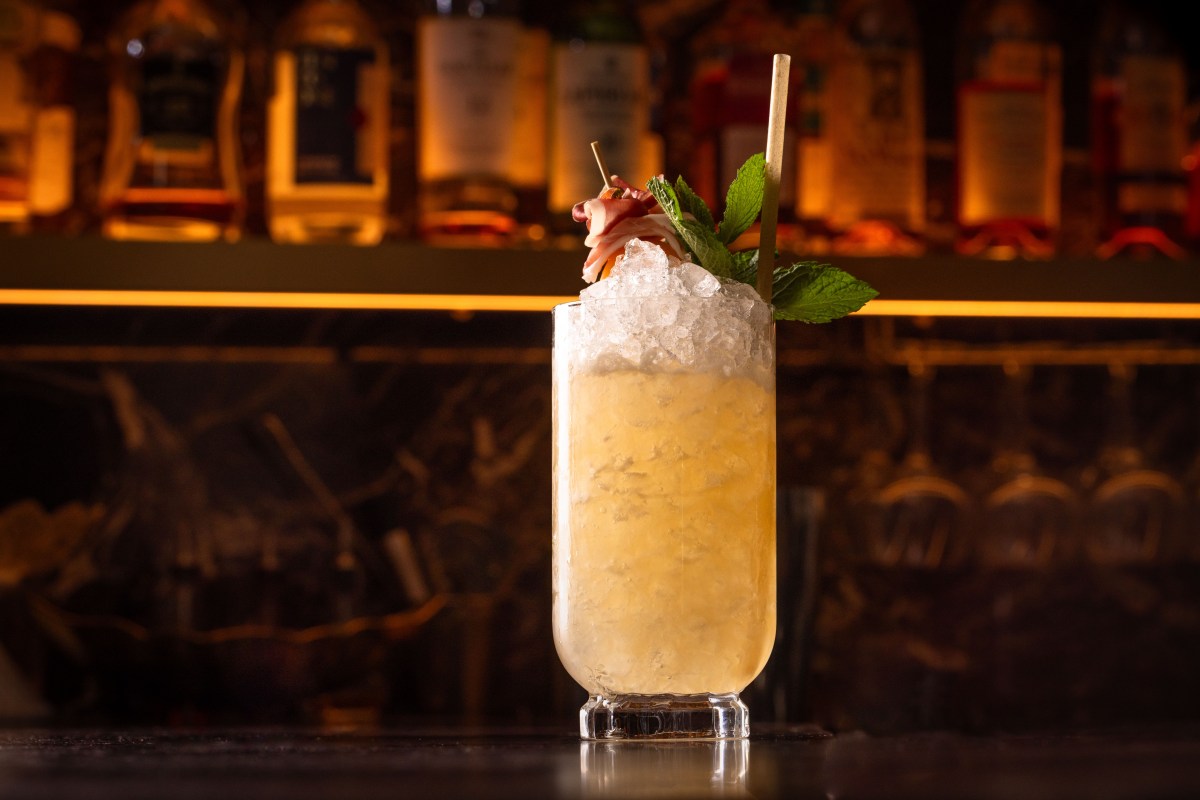 Cocktail with mint and prosciutto garnish on the restaurant's dark marble bar, bottles in background