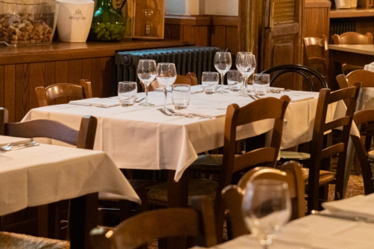 Dining room with wood-paneled walls, set tables with white linens, wine glasses and wooden chairs.