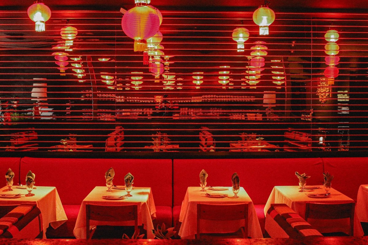 Red-lit dining room with paper lanterns, mirrored shelving, and white-clothed tables set for service