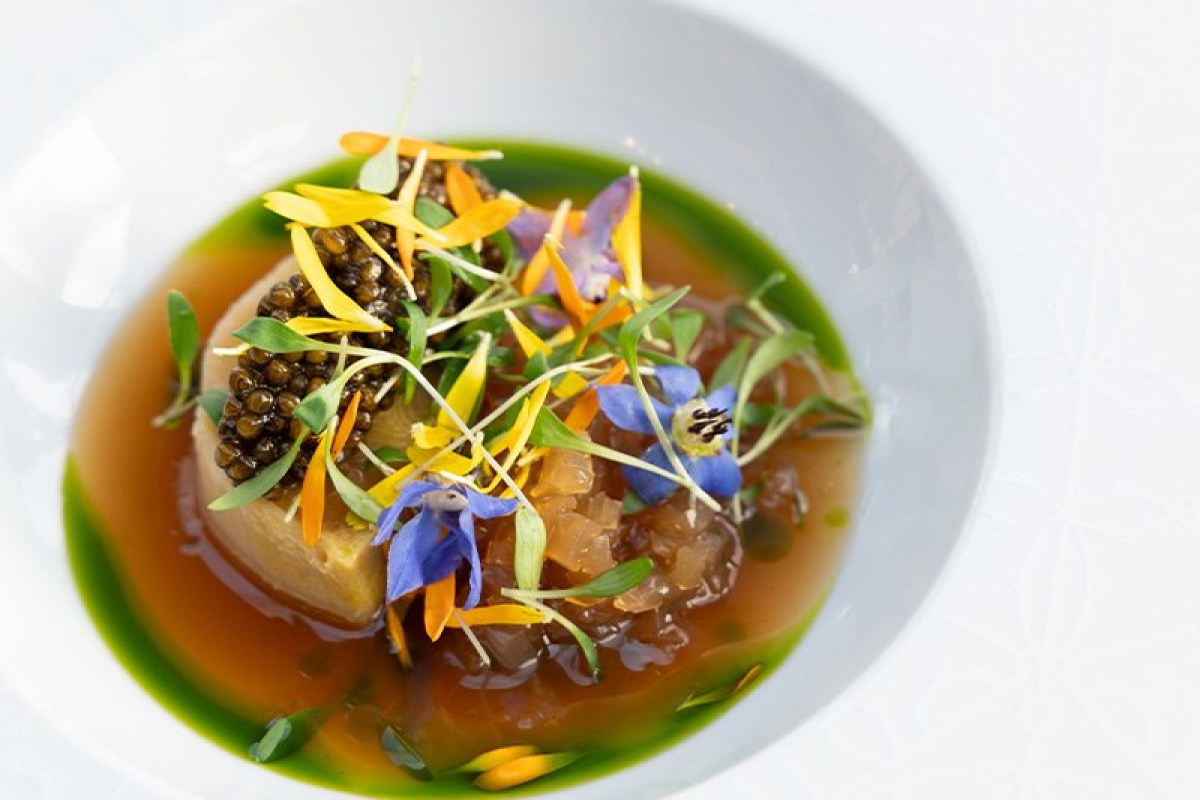 Elegant plated dish with caviar, edible flowers and herbs in a light broth