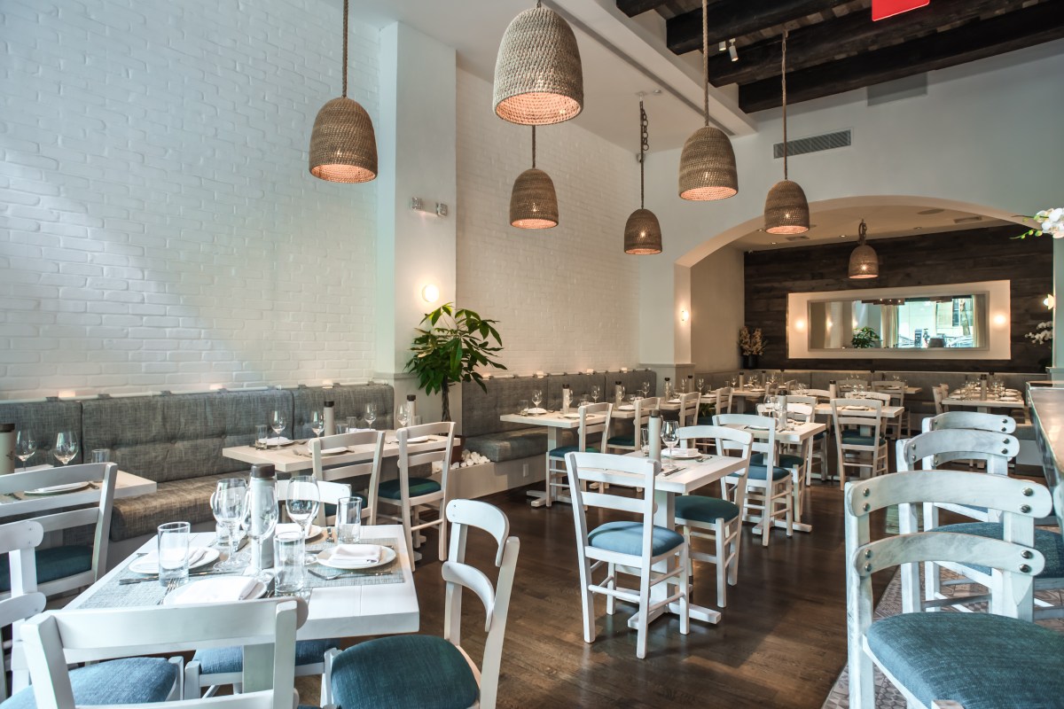 Bright dining room with white brick walls, wicker pendant lights, and blue-cushioned chairs at set tables