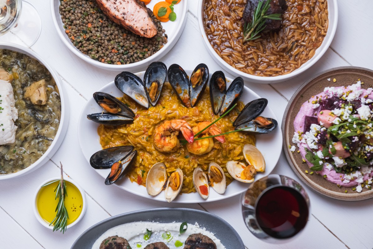 Overhead view of a spread of Mediterranean dishes including seafood rice, salmon, lentils, and beet salad