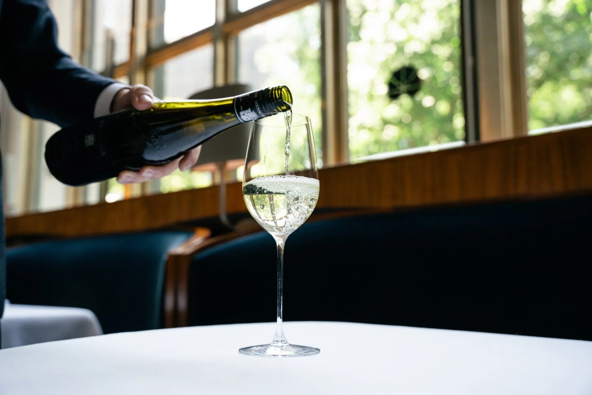 Wine being poured into a glass at a table near large windows in the dining room