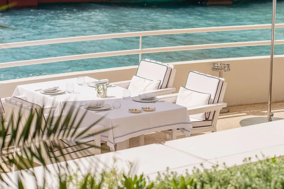 Terrace table set for dining overlooking turquoise sea, white tablecloth and chairs at Elsa Marcel Ravin