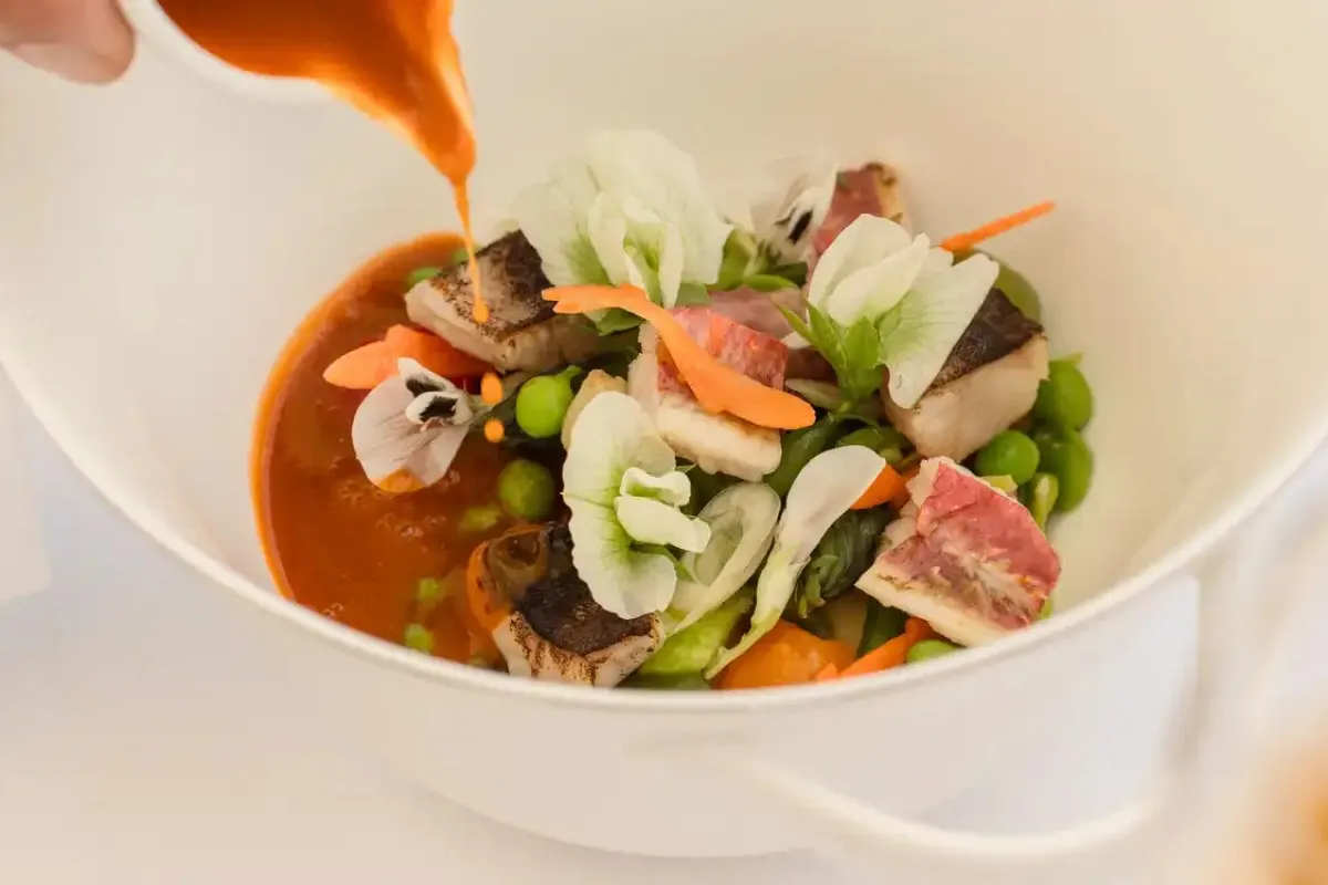 Elegant plated dish with fish, peas, edible flowers and orange sauce being poured, fine dining presentation