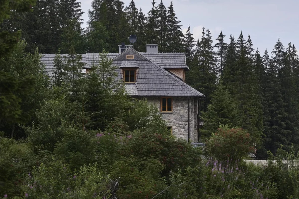 Stone and wood hotel building with shingled roof surrounded by pine forest and greenery