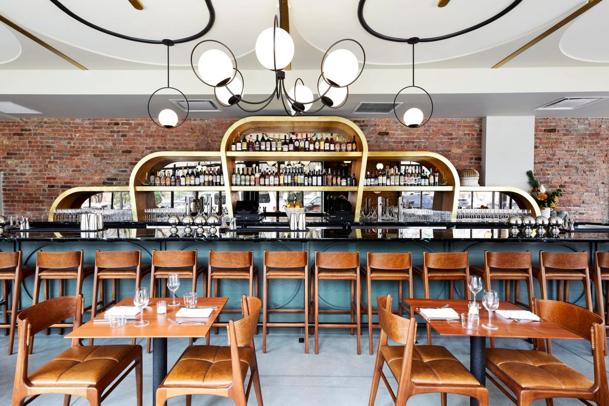 View of the bar area with brass shelving, bottles, and leather bar stools at Ernesto's