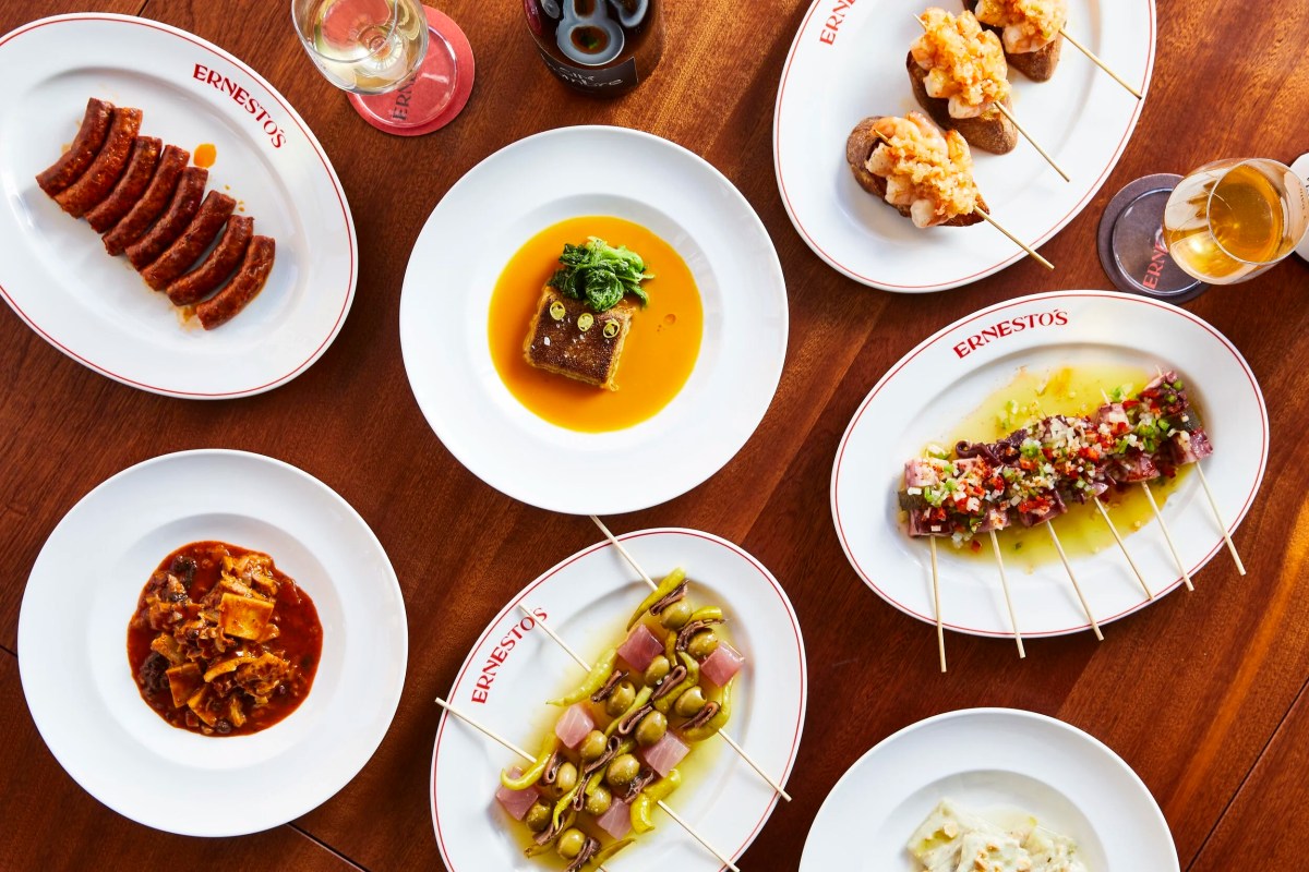 Overhead view of assorted tapas dishes on Ernesto's branded plates with wine glasses