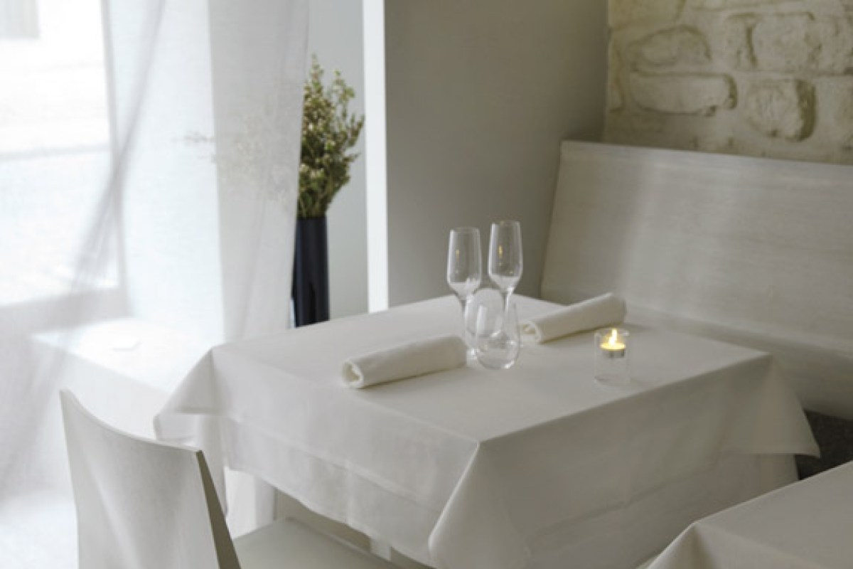 Close-up of a set table with wine glasses, folded napkins and candle by a stone wall