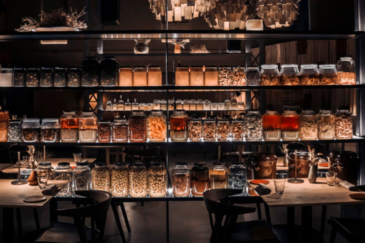 Close view of illuminated shelving filled with jars of preserved foods above restaurant dining tables