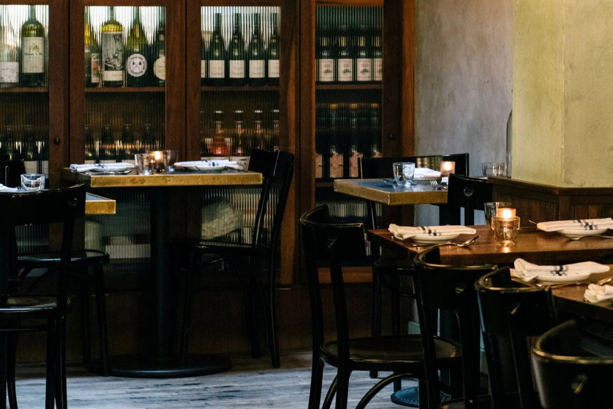 Restaurant dining room with wine cabinet, dark wood tables set with napkins and candles