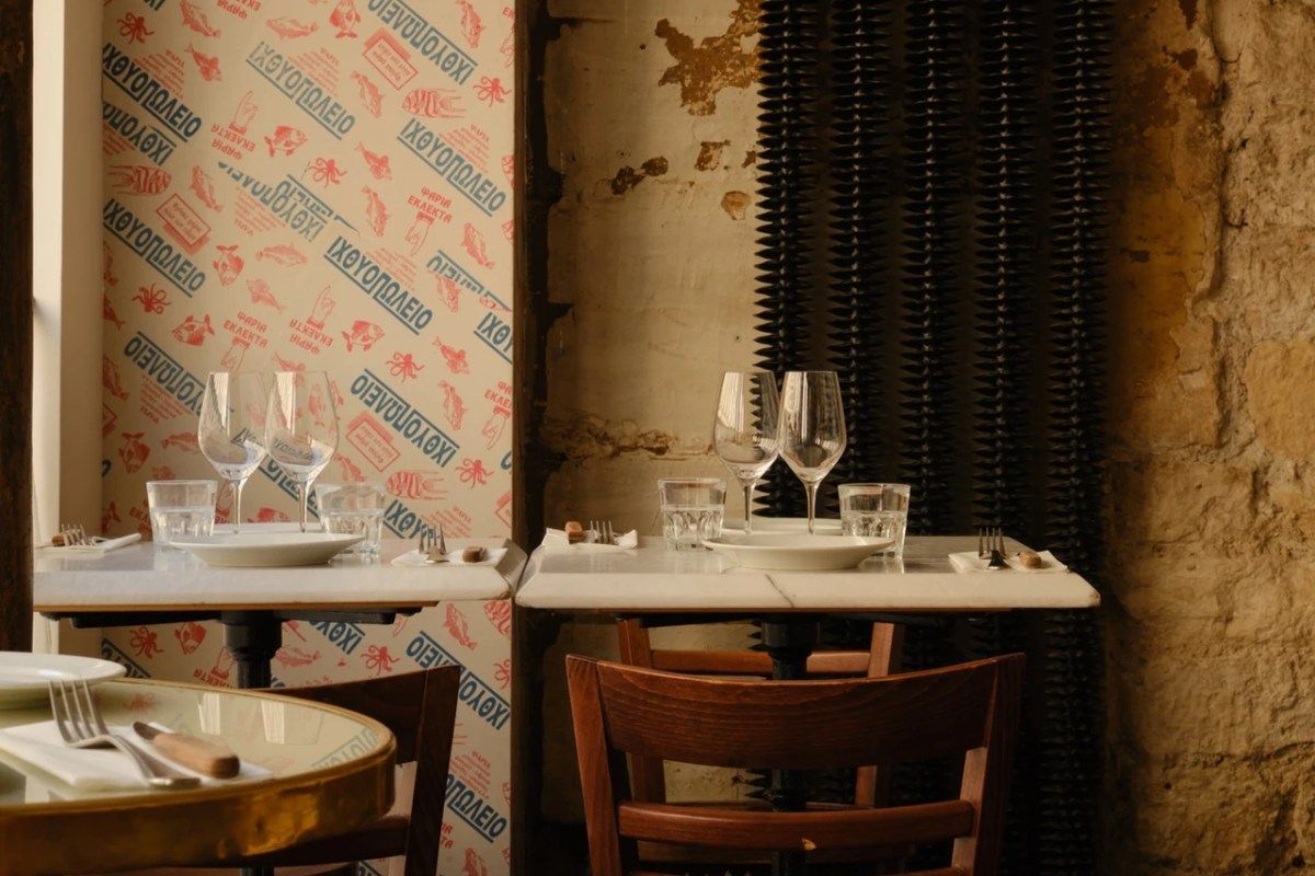 Restaurant dining room with marble tables, wine glasses set, patterned wallpaper and exposed stone wall