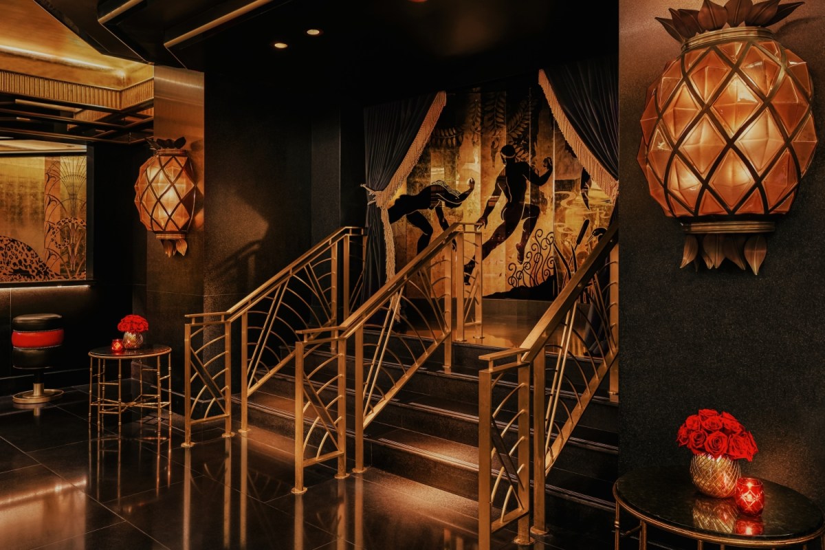 Hotel lounge area with gold art deco staircase, pineapple lamps, and mural of dancers